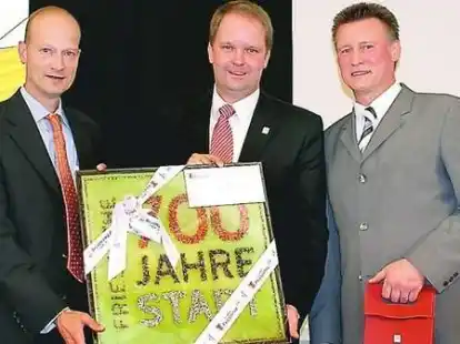 B&uuml;rgermeister Johann Wimberg gratuliert mit dem Jubil&auml;umsbild dem Friesoyther Gesch&auml;ftf&uuml;hrer Willehard Plaggenborg (r.) und Firmeninhaber Hermann G&uuml;th (l.).