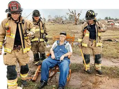 Gene Tripp sitzt inmitten von Feuerwehrm&auml;nnern in einem Schaukelstuhl. Sein Haus in Oklahoma wurde zerst&ouml;rt.
