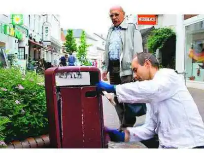 Interessierte Beobachter Kay Mensing (r.) r&uuml;ckt derzeit in der Innenstadt M&uuml;lleimern, Fahrradst&auml;nder, B&auml;nken und Stra&szlig;enlaternen mit Stahlb&uuml;rste und Farbe zu Leibe. Das interessiert auch die Vareler, die oft stehen bleiben.