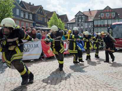 Ein Team in Feuerwehr-Montur zieht  beim Buspulling einen Reisebus &uuml;ber den Stadtplatz in Wolfenb&uuml;ttel.