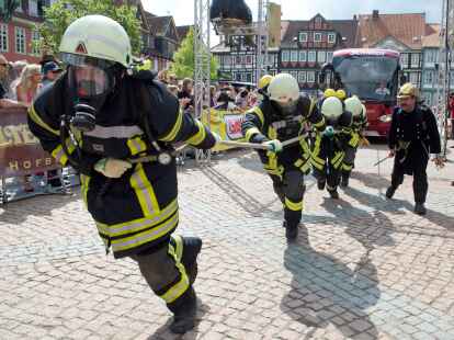 Ein Team in Feuerwehr-Montur zieht  beim Buspulling einen Reisebus &uuml;ber den Stadtplatz in Wolfenb&uuml;ttel.