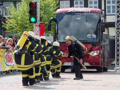 Ein Team in Feuerwehr-Montur zieht  beim Buspulling einen Reisebus &uuml;ber den Stadtplatz in Wolfenb&uuml;ttel.