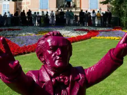Hinter einer Plastik-Figur des K&uuml;nstlers Ottmar H&ouml;rl, die den Komponisten Richard Wagner darstellt, warten Besucher w&auml;hrend einer unplanm&auml;&szlig;igen Unterbrechung wegen technischen Defekts vor dem Festspielhaus.