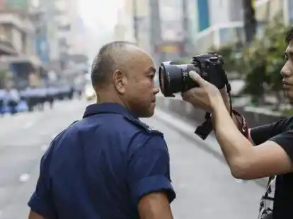 Ein Mann r&uuml;ckt einem Polizisten mit seiner Kamera auf die Pelle. Der findet das anscheinend wenig am&uuml;sant.