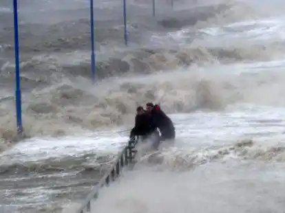 Zwei M&auml;nner halten sich am 05.12.2013 auf dem &uuml;berfluteten F&auml;hranleger in Dageb&uuml;ll (Schleswig-Holstein) an einem Gel&auml;nder fest.