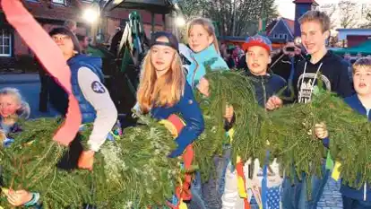 In Falkenburg packte  der Nachwuchs mit an: Nachdem die Junge Gruppe mit Trecker- und Muskelkraft den 18-Meter-Baum in die Vertikale gebracht hatte, halfen Kinder und Jugendliche (Bild) dem auf den Baum gekraxelten Eike Cordes beim Anbringen  des Gr&uuml;ns. Rund 300 G&auml;ste lie&szlig;en sich das Spektakel auf dem Dorfplatz nicht entgehen.