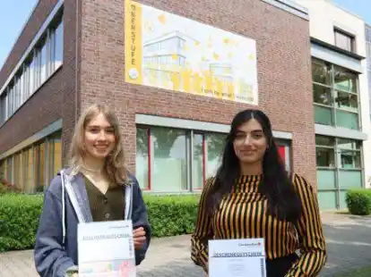 Die Siegerinnen des Wettbewerbs: Anna-Katharina Wordtmann und Maha Afzaal Mongia vor dem Banner an der Fassade des Oberstufengeb&auml;udes.