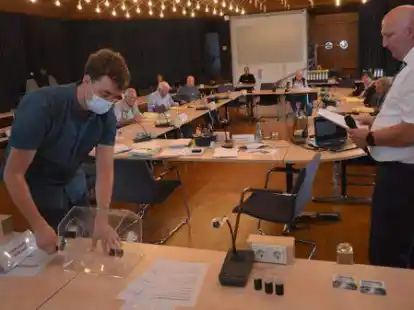 Bei Stimmengleichstand zweier Bewerber entschied das Los mit Stadtwahlleiter Helmut L&uuml;cht (rechts) und Gerold Josef Hoffmann an der Lostrommel. Das traf f&uuml;r Nachr&uuml;cker f&uuml;r den Rat zu. Im Hintergrund sind der Wahlausschuss und Zuschauer im Ratssaal zu sehen.