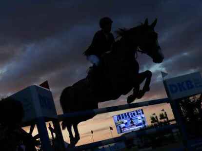 Ein Springreiter &uuml;berwindet mit einem Pferd ein Hindernis in der Abendd&auml;mmerung.