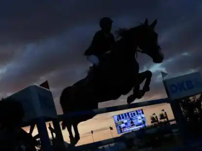 Ein Springreiter &uuml;berwindet mit einem Pferd ein Hindernis in der Abendd&auml;mmerung.