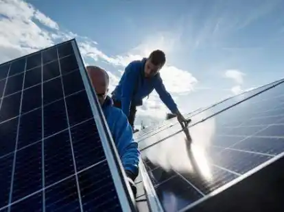 Mitarbeiter einer Firma montieren Photovoltaikmodule auf dem Dach eines Wohnhauses.