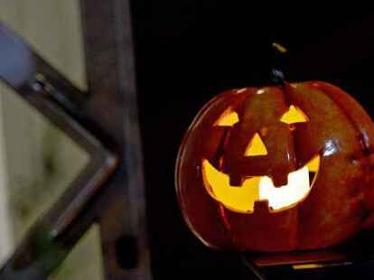 Halloween: Ein Dekok&uuml;rbis mit Gesicht leuchtet vor einer geschlossenen Haust&uuml;r.