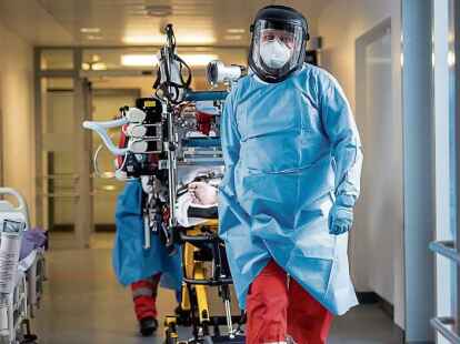 Das Team eines Intensivtransportwagens f&auml;hrt auf einer Intensivstation  einen Covid-19-Patienten auf einer Intensivtrage.