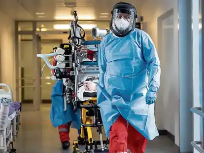 Das Team eines Intensivtransportwagens f&auml;hrt auf einer Intensivstation  einen Covid-19-Patienten auf einer Intensivtrage.