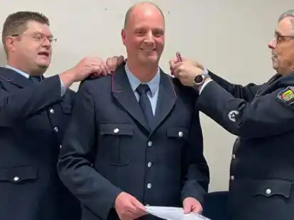Ortsbrandmeister Jens Onken (links) und Gemeindebrandmeister Peter Hoffbauer stecken Holger Kiefer die neuen Schulterklappen an.