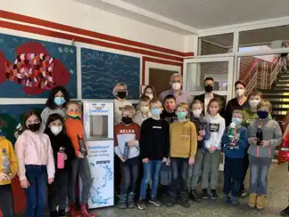 Die Klasse 4b der Grundschule (Vordergrund) sowie (Hintergrund, von links) Daniela Eick (Lehrkraft), Monika Meyer (Lehrkraft), Josef Niehaus (Schulleiter), J&ouml;rn Logemann (Projektleiter Niedersachsen Wasser) und Bettina Brack (F&ouml;rderverein) freuen sich &uuml;ber den Trinkwasserspender.