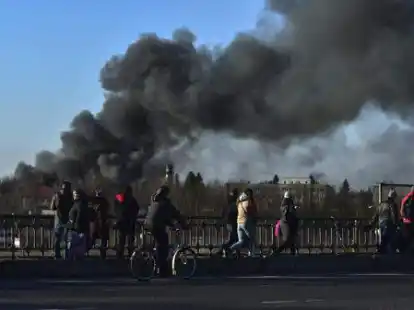 Menschen stehen auf einer &Uuml;berf&uuml;hrung und schauen auf eine Rauchwolke, die offenbar nach einer Raketen-Explosion in der N&auml;he des Flughafens der westukrainischen Gro&szlig;stadt Lwiw (Lemberg) aufsteigt.  Das Auricher Team von Dr. Wessels ist nicht weit entfernt.