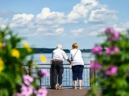 Ein Paar steht bei sch&ouml;nem Wetter am Ufer des Zwischenahner Meers an einem Gel&auml;nder und blickt auf das Wasser.