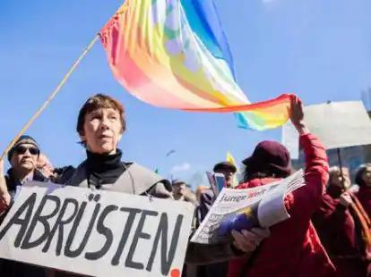 Ostermarsch in Berlin: Eine Frau tr&auml;gt am Oranienplatz in Kreuzberg eine Friedensfahne und ein &bdquo;Abr&uuml;sten&ldquo;-Schild.