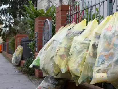 Gef&uuml;llte gelbe M&uuml;lls&auml;cke h&auml;ngen in einer Stra&szlig;e am Gartenzaun zur Abholung bereit (Symbolbild).