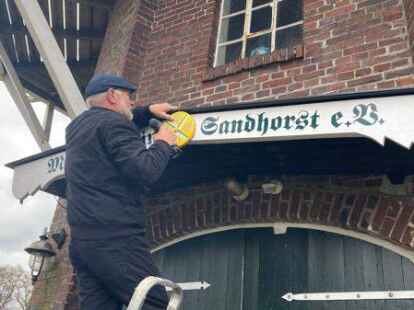 M&uuml;hlenwart Gerhard Poppen von der Sandhorster M&uuml;hle bei der Anbringung eines neuen Schilds von Kunstmaler Wolfgang V&ouml;lckner.