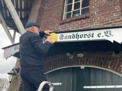 M&uuml;hlenwart Gerhard Poppen von der Sandhorster M&uuml;hle bei der Anbringung eines neuen Schilds von Kunstmaler Wolfgang V&ouml;lckner.