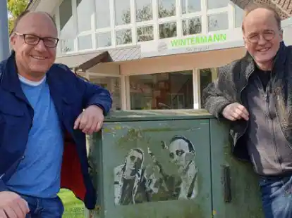 Gehen f&uuml;r ein &bdquo;Trio&ldquo;-Foto gern mal auf die Knie: Dirk Wintermann (links) und Ralf Kempermann an einem Stromverteilerkasten in Gro&szlig;enkneten. Dort prangt noch ein verblasstes Bild der drei Musiker, die einst in der Gemeinde Gro&szlig;enkneten wohnten.