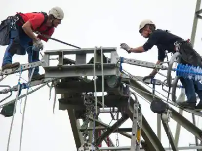Rund f&uuml;nfzig Meter &uuml;ber dem Boden stehen zwei Monteure auf dem Ausleger eines Strommastes.