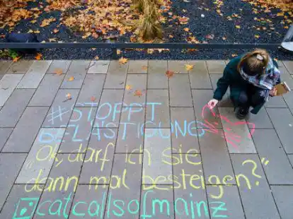 Themenbild: Melina Crispin, Aktivistin, schreibt mit Kreide einen anz&uuml;glichen Kommentar &bdquo;#Stoppt Bel&auml;stigung Ok, darf ich Sie dann mal besteigen? catcallsofmainz&ldquo; auf einen B&uuml;rgersteig in der Mainzer Innenstadt.