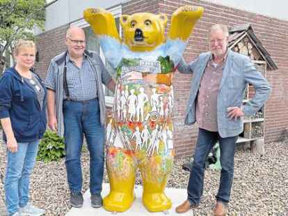 Der K&uuml;nstler Hans-Christian Petersen (rechts) pr&auml;sentiert Thomas Knauer und Liane Willms vom AWO-Altenwohnzentrum in Esens den neuen Buddy-B&auml;ren, den er gestaltet hat.
