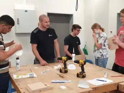 Hand angelegt: Tischlermeister Felix Siemer (Zweiter von links) und Auszubildender Jan-Hendrick Paschen (Mitte) erkl&auml;rten den Sch&uuml;lern Flit, Anna und Kevin die einzelnen Arbeitsschritte f&uuml;r den Handyhalter aus Holz.