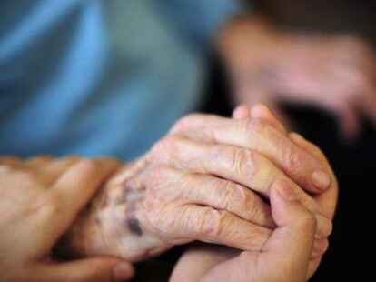 Eine Pflegekraft h&auml;lt in einem Seniorenheim die Hand einer Bewohnerin. Immer mehr Menschen engagieren sich in der ehrenamtlichen Sterbebegleitung.