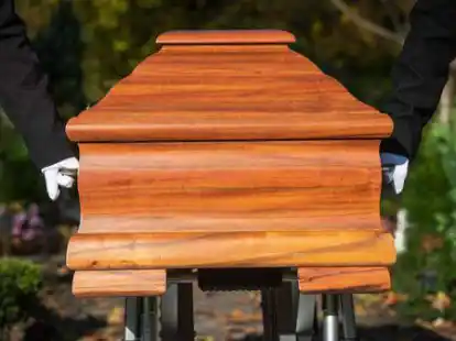 Sargtr&auml;ger schieben einen Sarg.