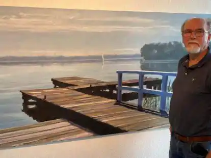 Galerist Puck Steinbrecher vor einem der ausgestellten Bilder:Es ist der DLRG-Steg am Zwischenahner Meer zu sehen, gemalt von Werner Heinze.