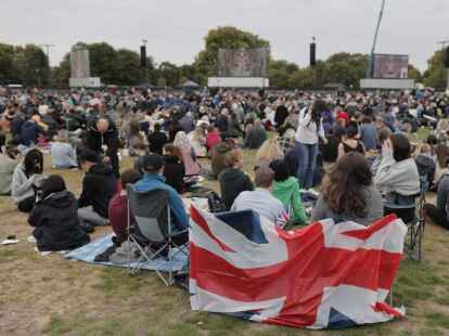London: Um die staatliche Trauerfeier der britischen Königin Elizabeth II. zu verfolgen, sitzen im Hyde Park mehrere Menschen um auf riesigen Bildschirmen.