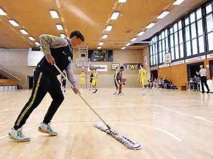 Wisch-Aktion: Juniors-Spieler Simon Kohlhoff beim Versuch, das rutschige Parkett in der Haarenufer-Halle so zu bearbeiten, dass gespielt werden kann.