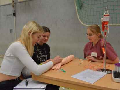 Gesundheits- und Krankenpflegerin Katharina Reimer (rechts) vom Klinikum Stenum &uuml;bte mit den Sch&uuml;lerinnen und Sch&uuml;lern an einem Kunstarm die Blutabnahme. BILD: Thilo Schr&ouml;der