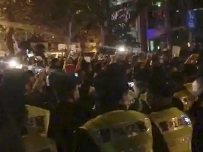 In diesem Bild aus einem Video, das The Associated Press erhalten hat, beobachtet die Polizei (im Vordergrund) die Demonstranten in Shanghai. In der Nacht zum Samstag kam es in mehreren St&auml;dten zu Protesten gegen Chinas restriktive COVID-Ma&szlig;nahmen, die von der Wut &uuml;ber einen t&ouml;dlichen Wohnungsbrand in der westlichen Region Xinjiang angefacht wurden.