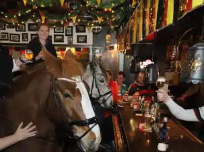 Pferde vor der Theke: Kultwirt Jan Lange (wei&szlig;es Trikot) prostet den beiden Reiterinnen Natascha Deters (links) und Lorena Ebkens mit ihren Pferden vor der Theke zu.