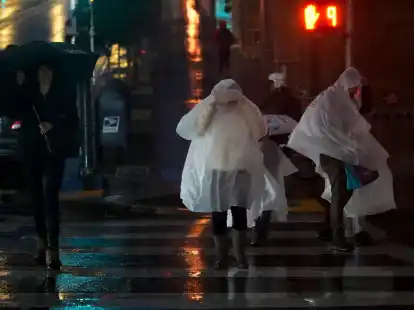 Menschen in Regenponchos &uuml;berqueren eine Stra&szlig;e in San Francisco.