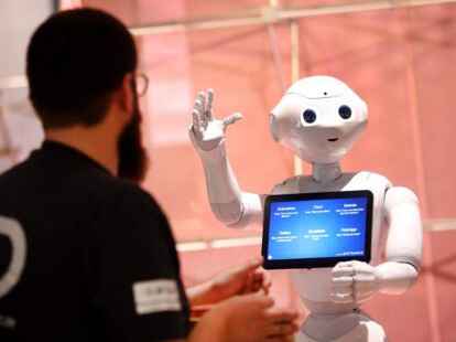 Der humanoide Roboter „Pepper“ kommuniziert mit einem Fachbesucher einer Sonderausstellung zum Thema „Künstliche Intelligenz“.