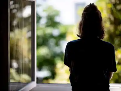 Eine Frau steht in ihrer Wohnung an einem Fenster. Die Zahl der Menschen, die sich wegen psychischer Erkrankungen krankmelden, nimmt zu.