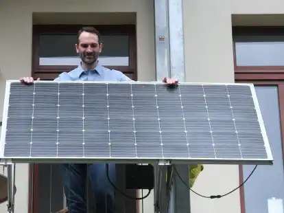 Ein Mann steht auf dem Balkon seiner Wohnung hinter einem Solarmodul. Der Boom bei sogenannten Balkon-Kraftwerken h&auml;lt an.