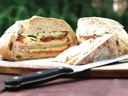 Was f&uuml;r eine praktische Idee: Ein rundes Wei&szlig;brot wird ausgeh&ouml;hlt und wahlweise mit Salami, Cheddar, Schinken, Salat und Tomaten gef&uuml;llt. Beim Picknick l&auml;sst es sich dann wie ein Kuchen in St&uuml;cke schneiden.
