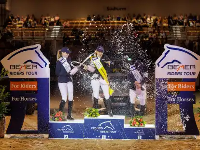 Janne-Friederike Meyer-Zimmermann (M) wird bei der Siegerehrung von Sophie Hinners (l) und Mathias Norheden Johansen mit einer Sektdusche gefeiert.