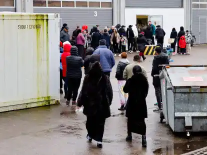Menschen stehen bei einer Essenausgabe in der Landesunterkunft der Gemeinde Seeth im Kreis Nordfriesland Schlange.