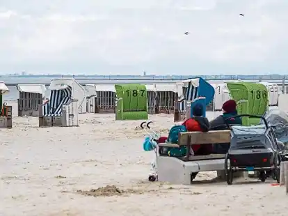 <p> Touristen sitzen zwischen Strandk&ouml;rben auf einer Bank am Strand von Norddeich. </p>