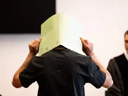 Der Angeklagte (M) verbirgt im Gerichtssaal sein Gesicht hinter einer Aktenmappe.