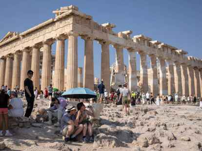 Eine Touristin trinkt Wasser unter einem Sonnenschirm in der Hitze von Athen.