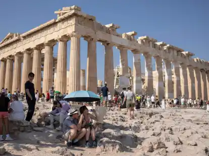 Eine Touristin trinkt Wasser unter einem Sonnenschirm in der Hitze von Athen.